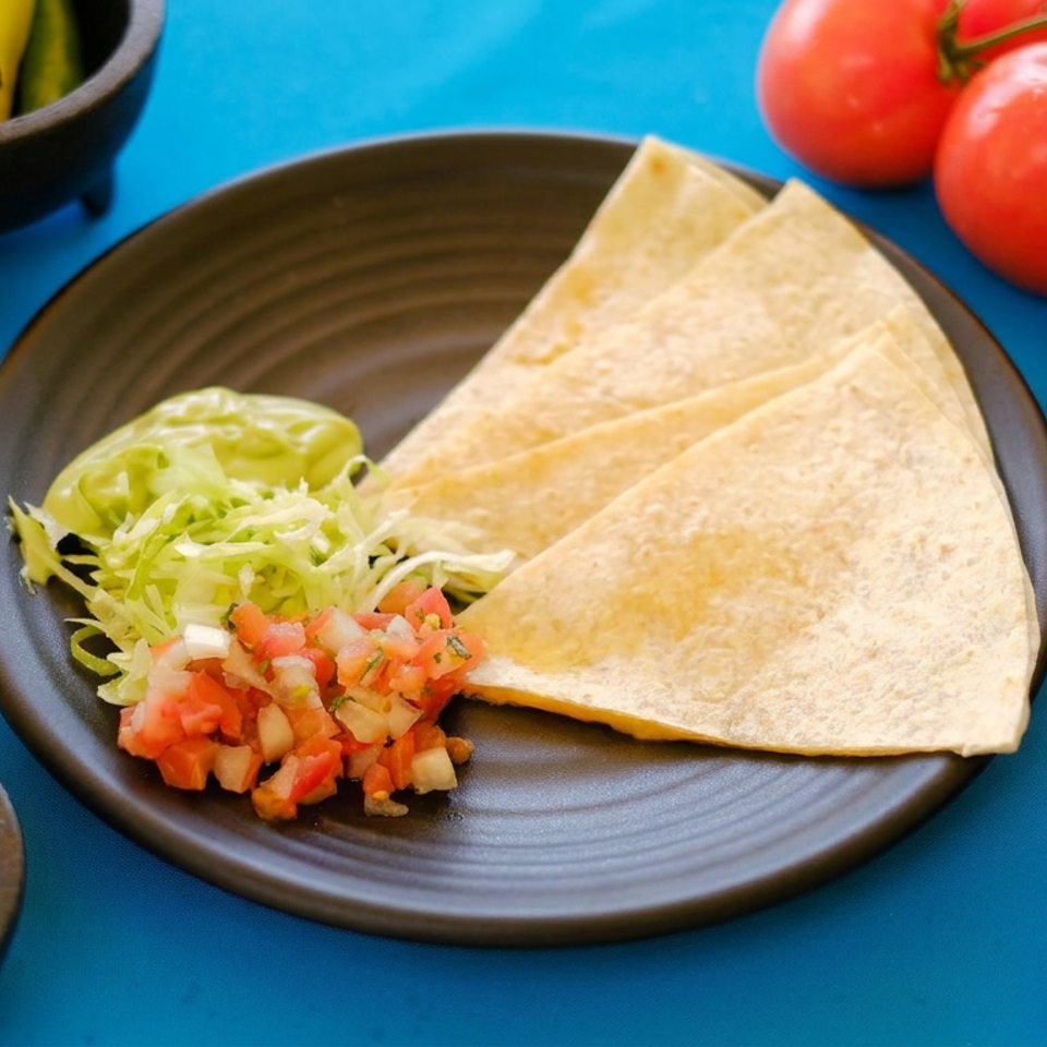 Plate of folded quesadillas with shredded lettuce and pico de gallo, surrounded by limes, chilies, tomatoes, and salsa.